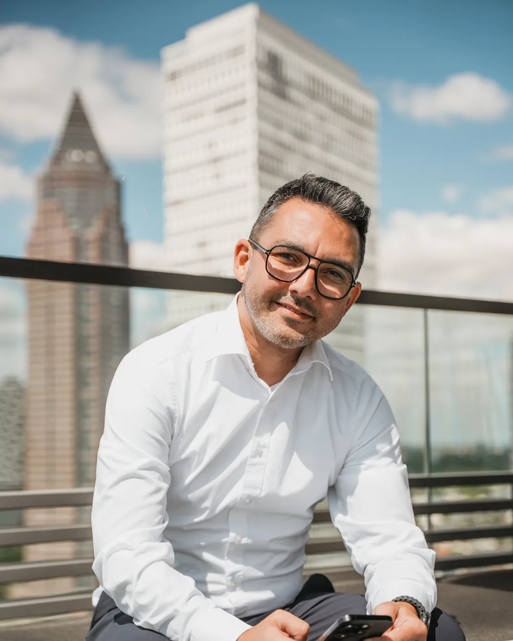 Batu Karaoğuz sitting on a roof terrace in front of the Frankfurt skyline