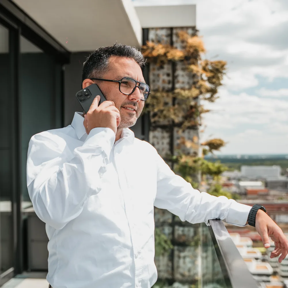 Batu Karaoğuz on the phone on a balcony above Frankfurt